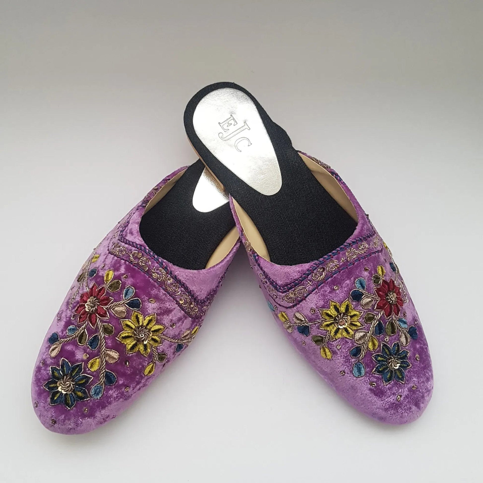 Pair of purple slippers with floral embroidery on a light gray background