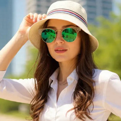 Woman wearing a white shirt and hat with green sunglasses in an urban park setting
