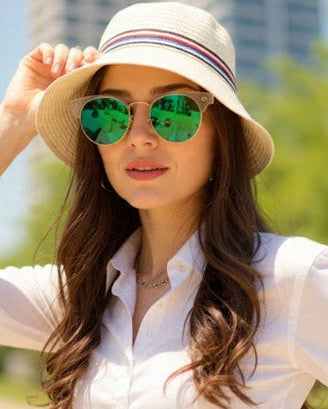 Woman wearing a white shirt, green sunglasses, and a beige hat with a blurred cityscape background